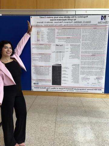 Grace Van Etten '27, in black pants, black top and pink blazer, shows off her poster at the UMass Chan Medical School Summer Undergraduate Research Program.